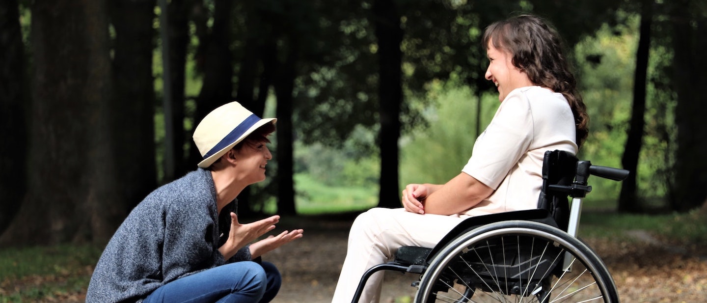 Foto: Frau im Rollstuhl sitzend und Freundin lachen miteinander im Gespräch